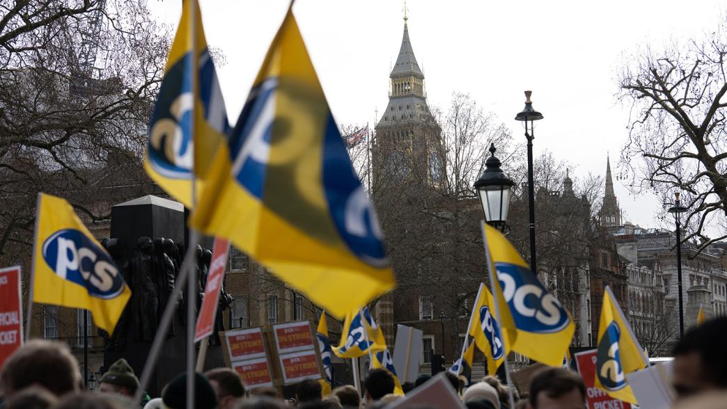 Striking civil servants holding PCS Union flags and marching past Westminster.