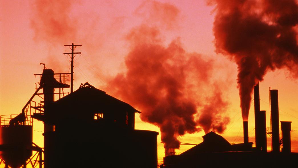 Silhouette of factory with chimneys emitting smoke, sunset 