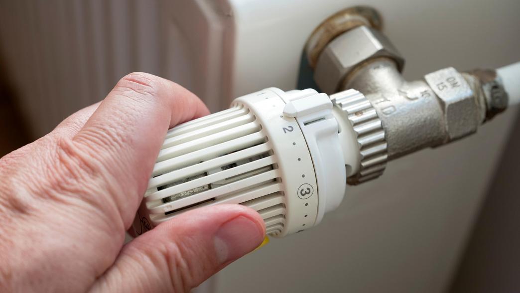 Person turning down the thermostat on a radiator