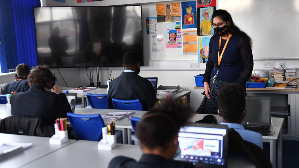 A teacher wears a facemask while teaching a primary school class
