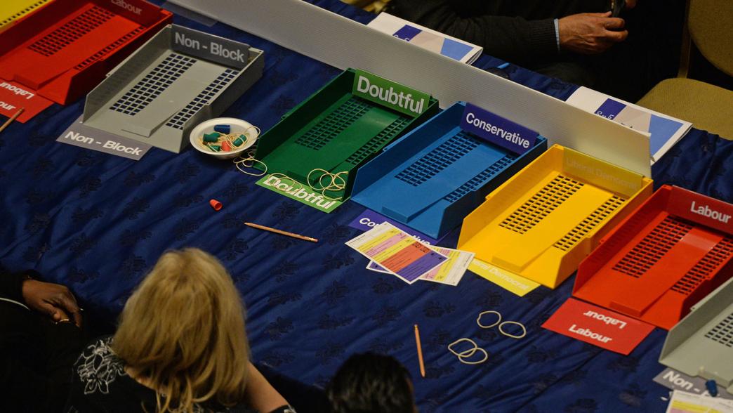 An image of election counting, with trays for each party including Labour, Conservative and the Lib Dems on the table.