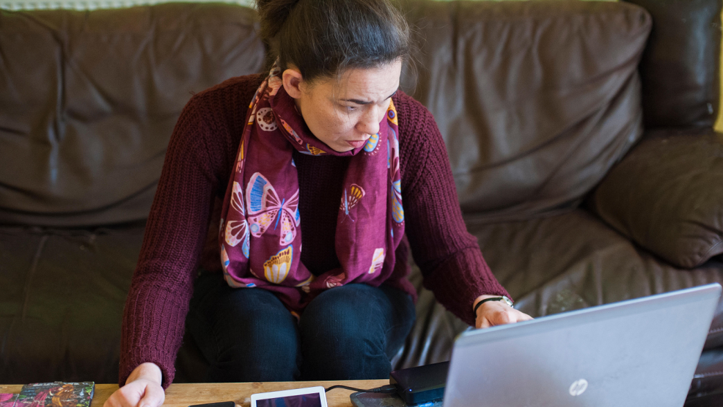 A woman in a burgundy jumper and floral scarf. In front of her is a laptop. 