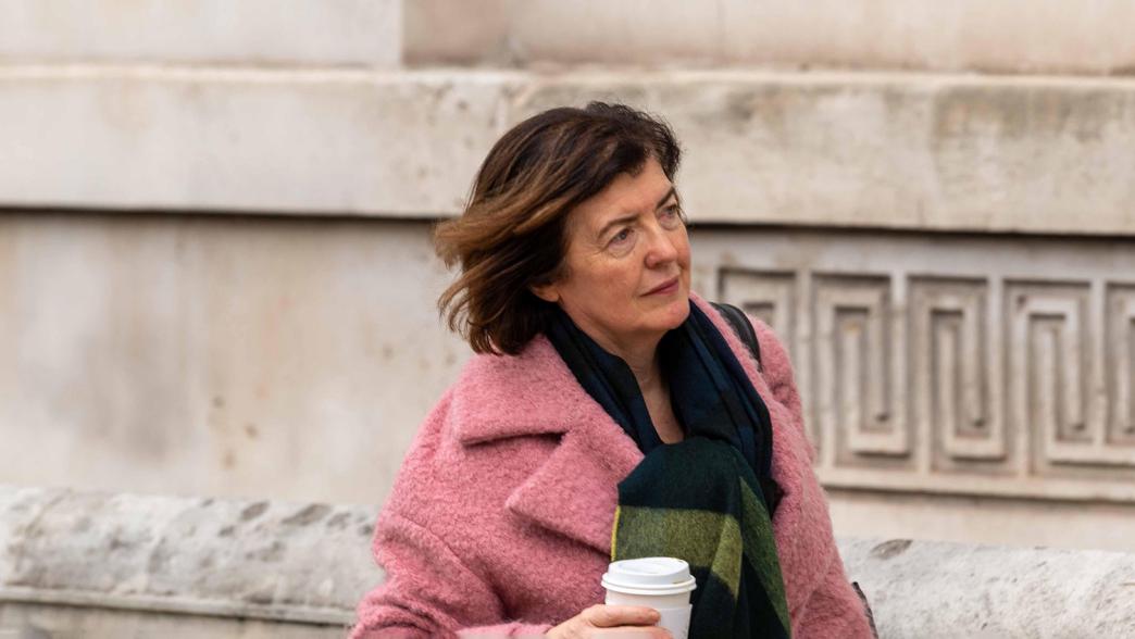 Sue Gray, senior civil servant, walking through Whitehall. She is wearing a pink coat and is carrying a coffee cup.