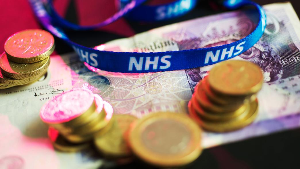 A concept of NHS funding with £20 pound notes and pound coins and an NHS lanyard