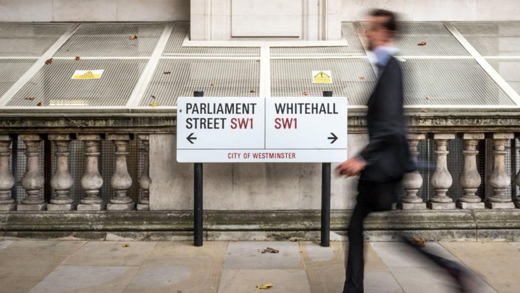 A man walking past the parliament/Whitehall road sign