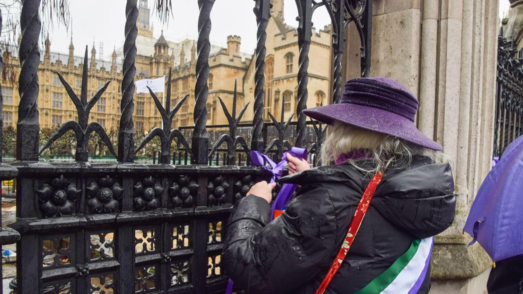 A WASPI protester ties ribbons on the fence outside parliament.