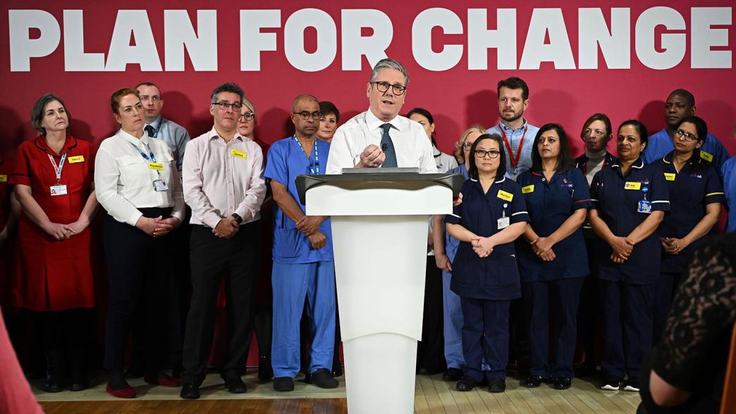 Keir Starmer giving a speech. Behind him are NHS staff and the backdrop says 'Plan for Change'.