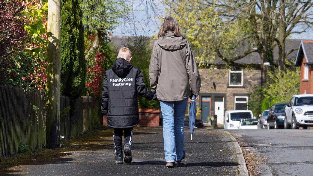 A woman and a child walking outside. The child is wearing a coat which says Foster Families