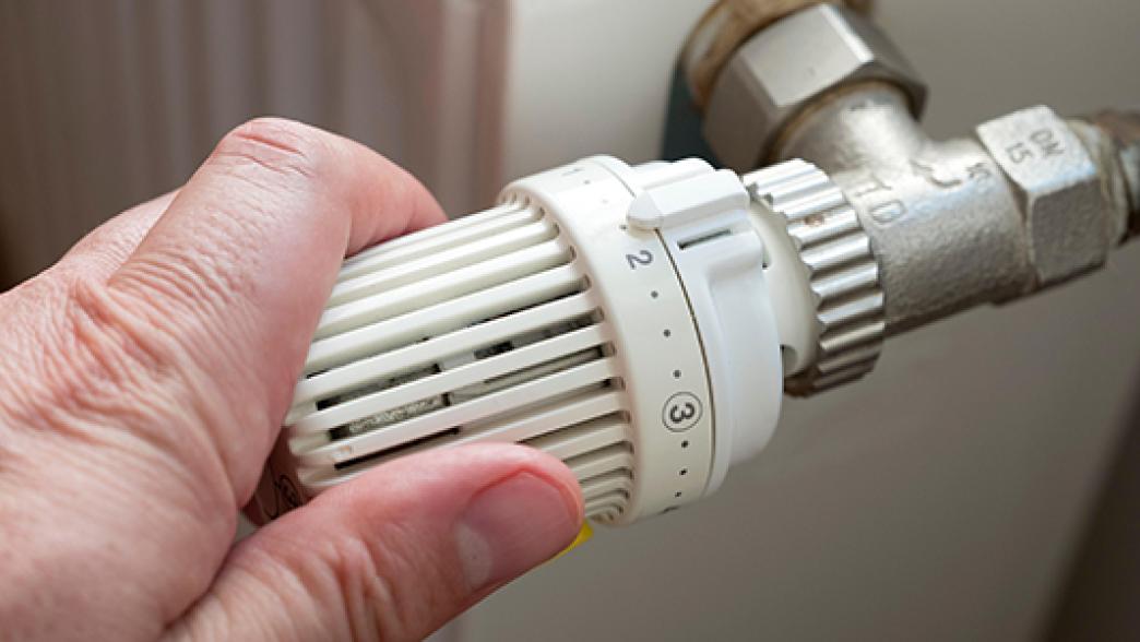 Man turning down thermostat on gas powered central heating radiator to save energy