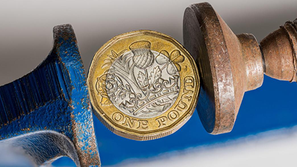 Pound sterling coin being squeezed between the jaws of a large vise