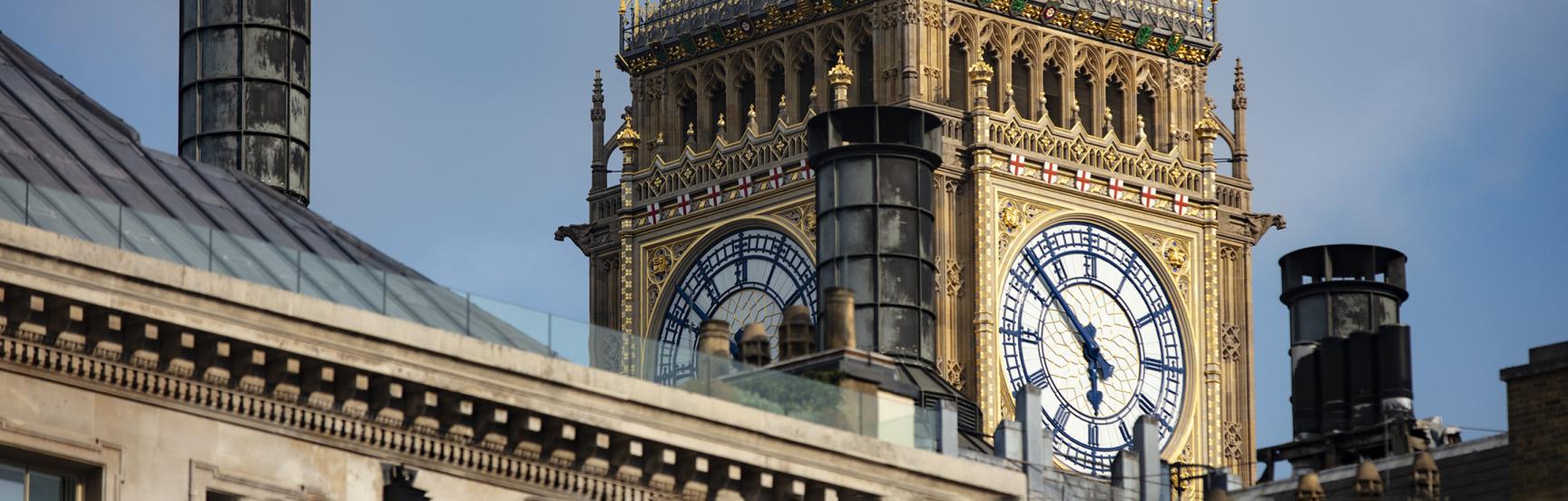 View of the Big Ben clock behind a building roof