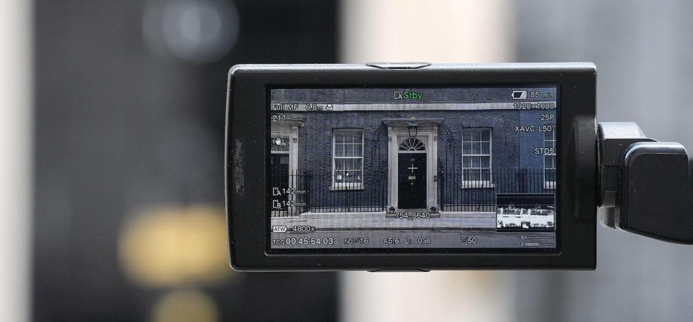 A screen of a TV camera pointing at the 10 Downing Street door is standing in the street in London