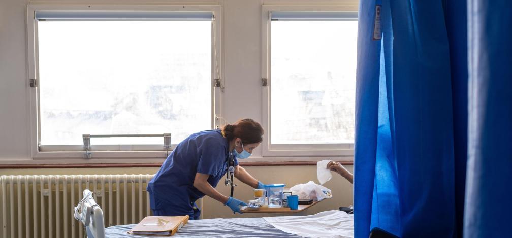 An NHS worker speaks to a patient in bed on the ward.