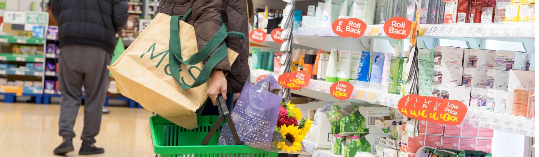 A woman carrying a supermarket shopping basket looking at reduced priced items.