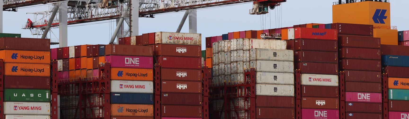 A close up of the deck of a large cargo ship docked in a British port being loaded with freight shipping containers which are being stacked by cranes