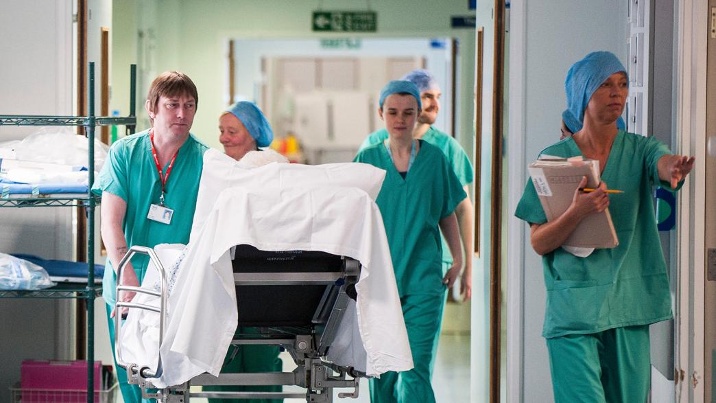 NHS staff wheeling a patient through the hospital corridor