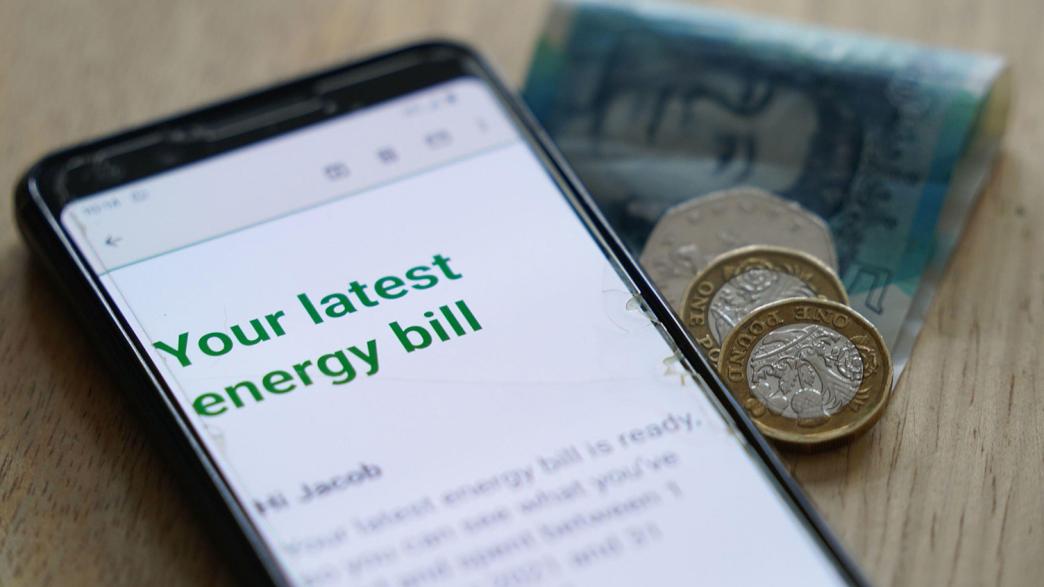 An online energy bill on a mobile phone with £7.50 in change next to it. 