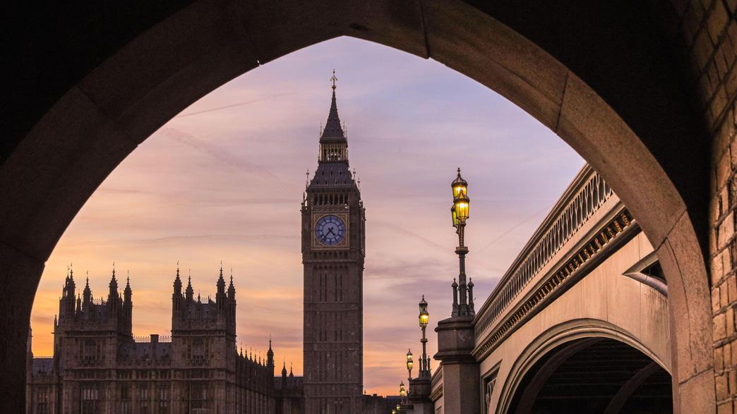 Big Ben and Houses of Parliament on the Thames are silhouetted against the sky and setting sun.
