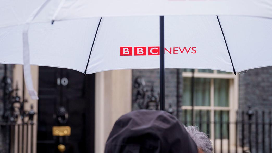 Someone holding a BBC News umbrella while standing outside Downing Street.