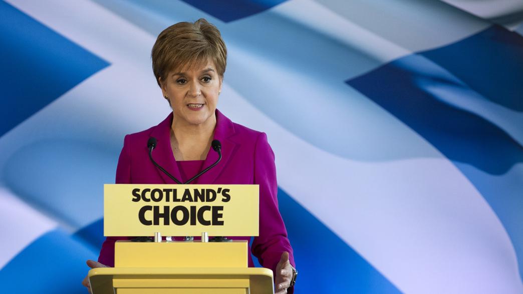 Nicola Sturgeon, standing in front of a Scottish flag background. She is behind a podium which says 'Scotland's Choice'.