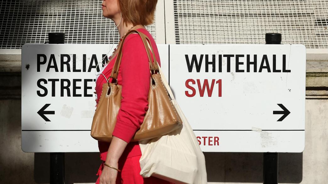 A woman walking past a road sign for Parliament Street and Whitehall.